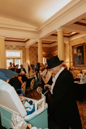 Guests browse items at a buffet table in an elegant room with classical columns and ornate decor.