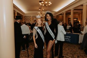 Three pageant contestants pose together at an indoor event with chandeliers visible in the background.