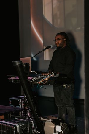 DJ performing on stage with electronic equipment in dark lighting conditions.