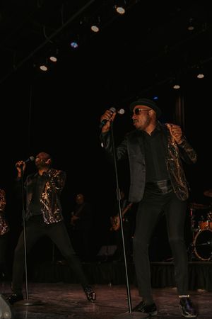 Performers on a dark stage with microphone stands silhouetted against dramatic lighting.