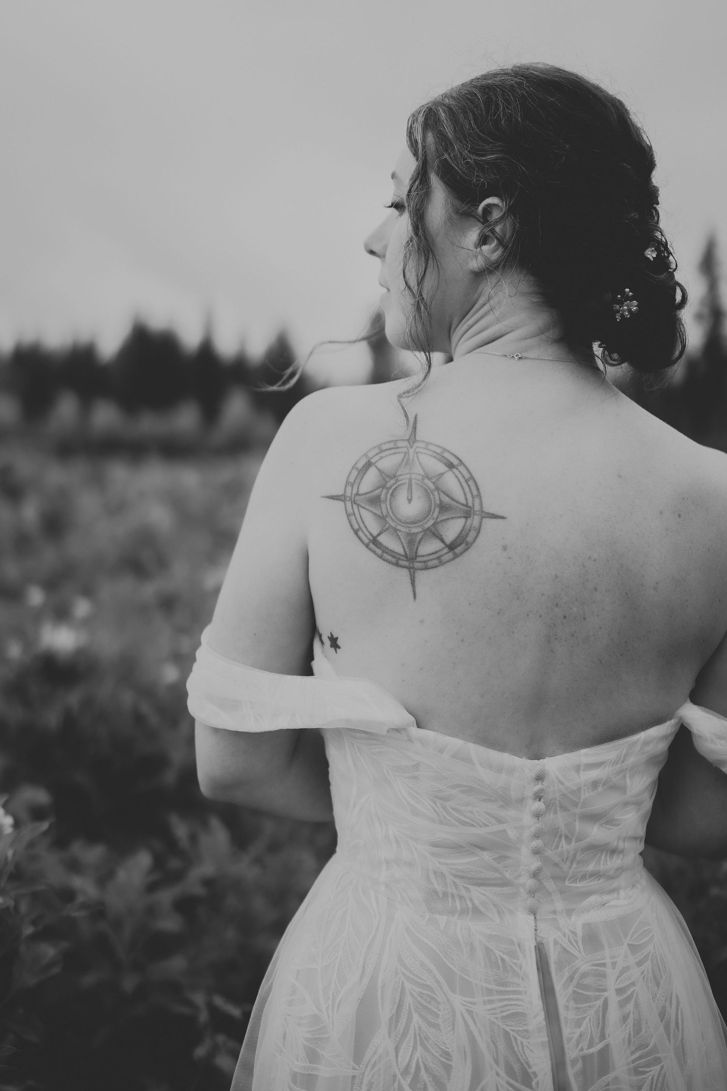 Black and white photo showing a compass rose tattoo on a person's back wearing a white wedding dress.