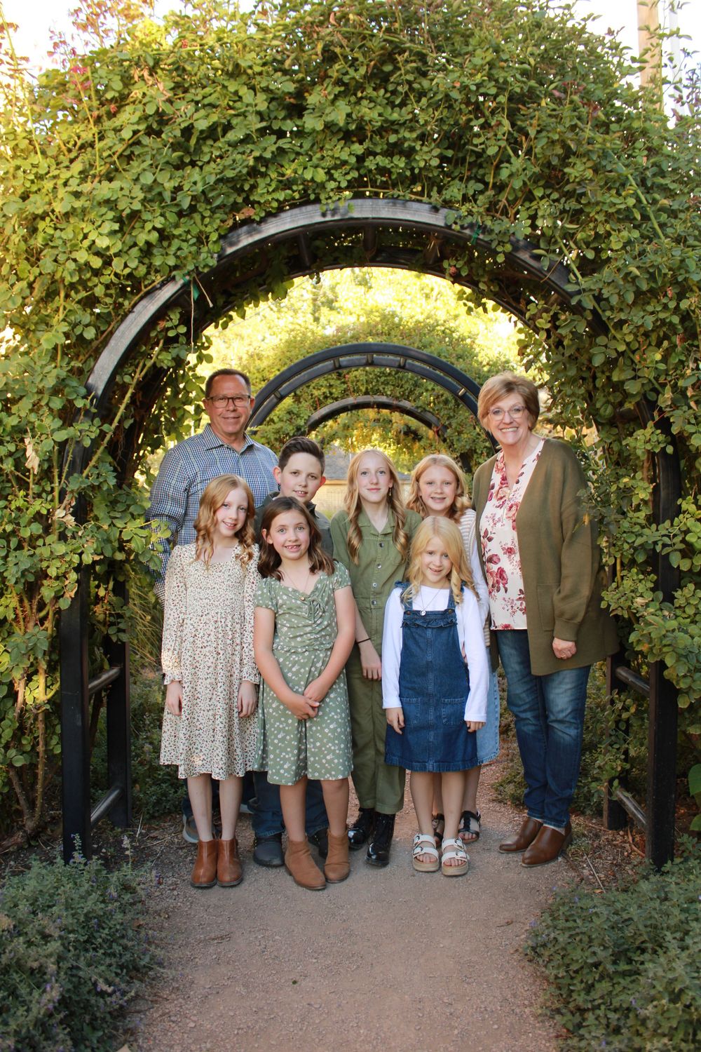 People gather under a garden archway covered in green foliage for a family portrait.