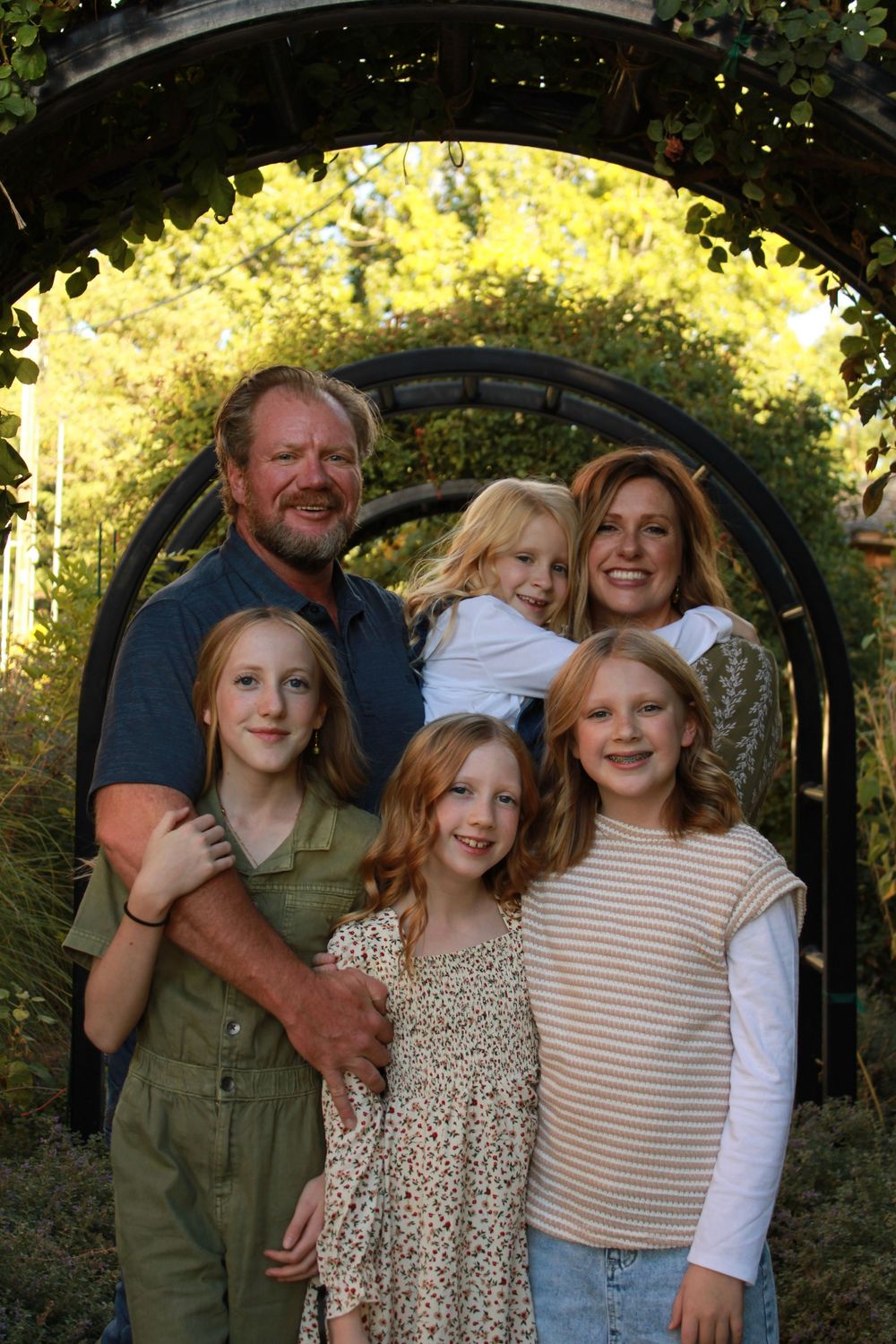 Family portrait session outdoors with group wearing coordinated casual outfits in earth tones against greenery.