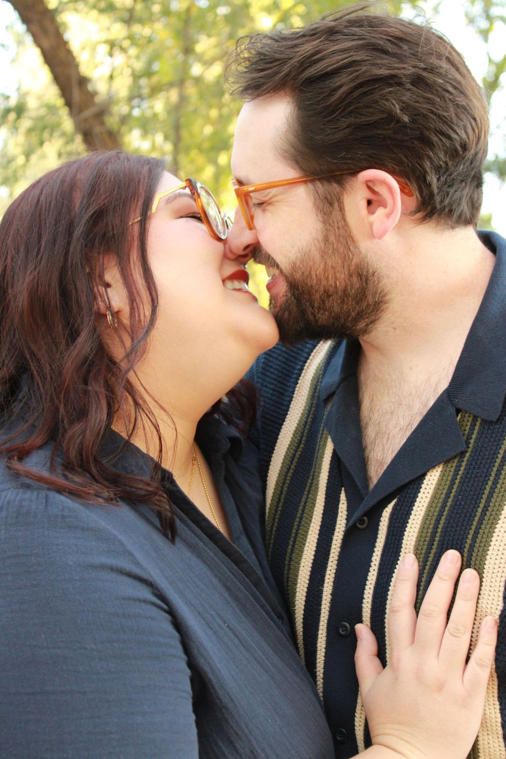 A romantic couple sharing an intimate moment outdoors with sunlit trees in the background.