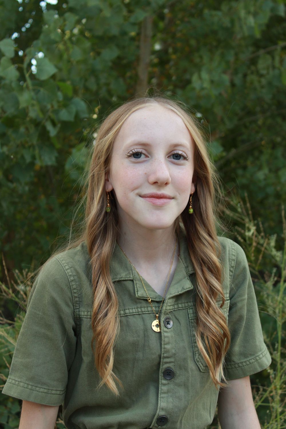 Portrait series of child in olive green button-up shirt against natural foliage background.