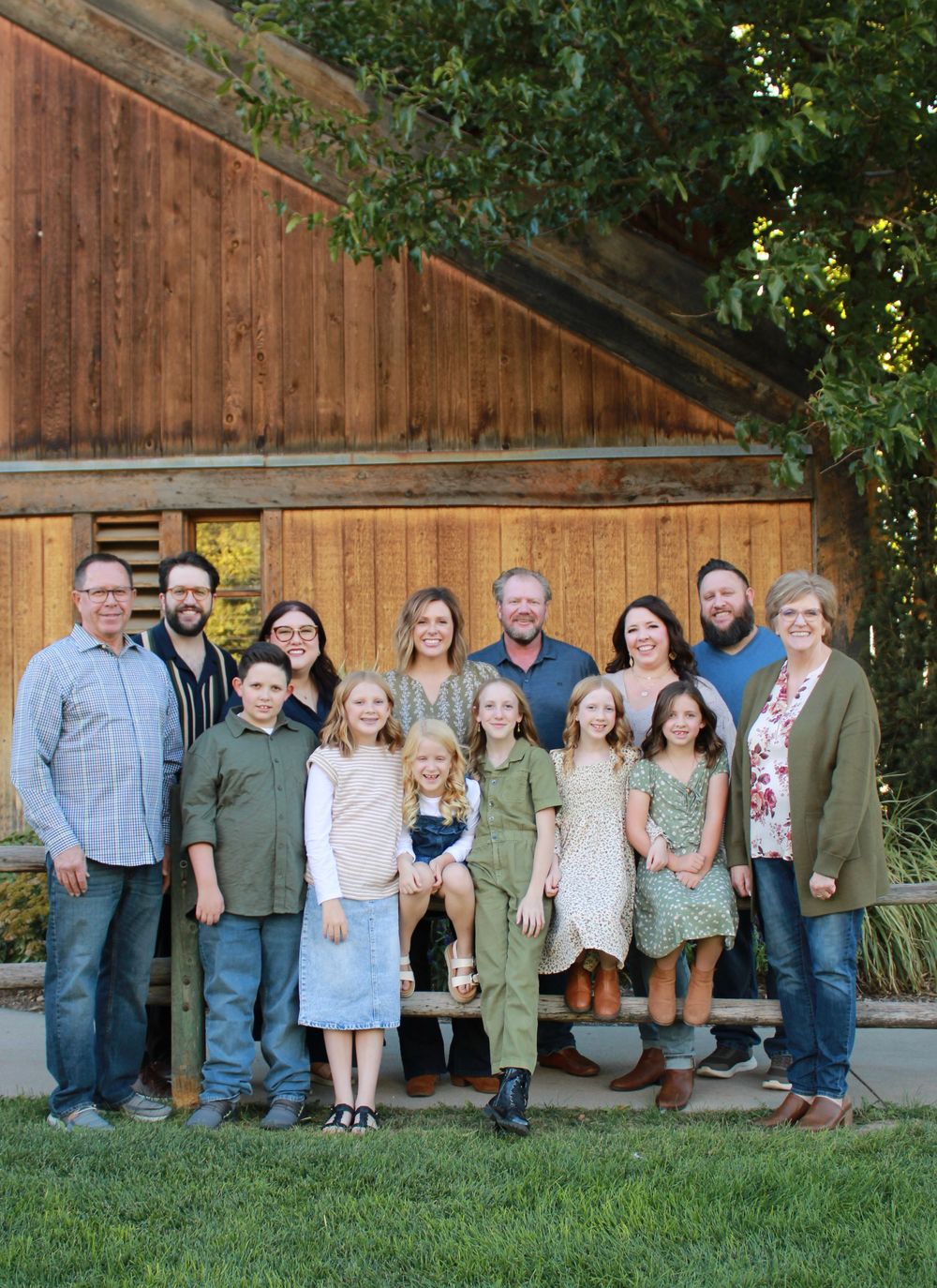 A group poses together in front of a rustic wooden barn wall during an outdoor photo session.