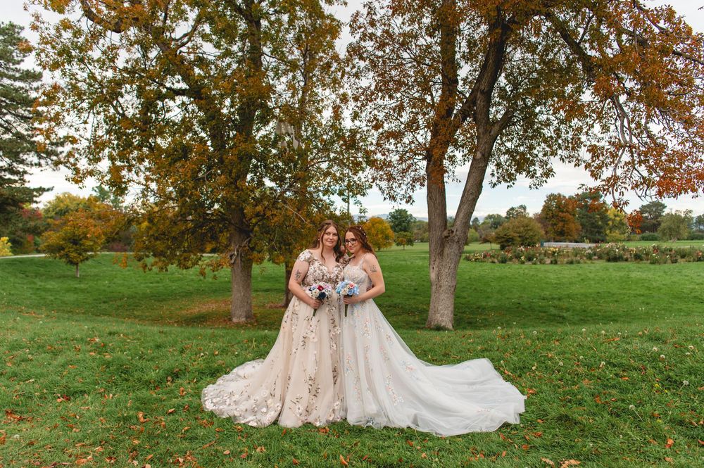 Wedding party in bright blue dresses and white gown pose together under autumn trees in a grassy field.