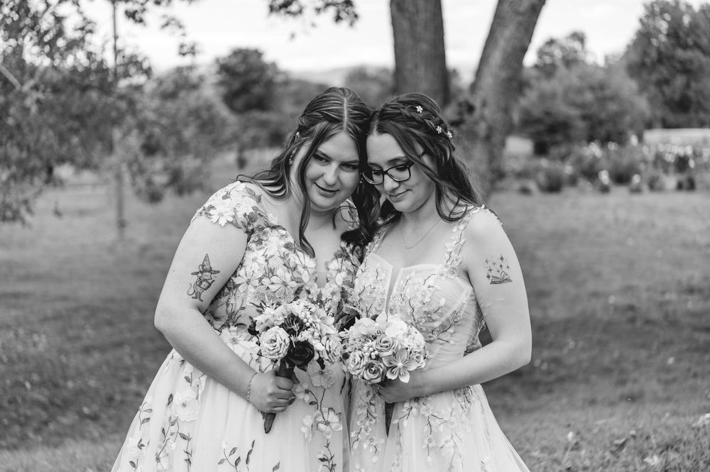Two people in white dresses embrace outdoors in a romantic garden setting during a wedding celebration.
