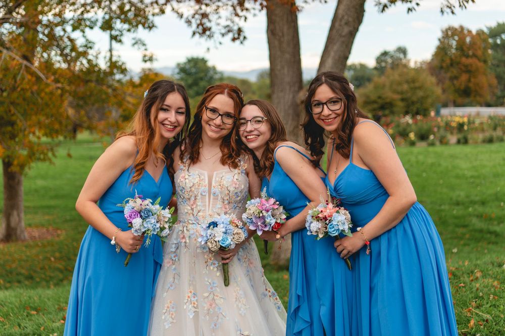 Bridesmaids in bright blue dresses and bride in white gown pose together in autumn outdoor setting.