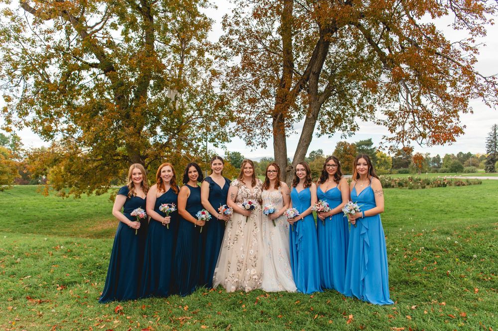 Wedding party in blue and beige dresses poses together on a grassy hill during autumn.