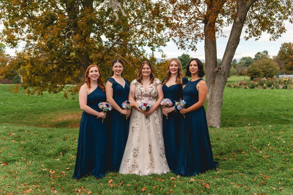 Wedding party in navy blue bridesmaid dresses and champagne bridal gown pose together on autumn grass.