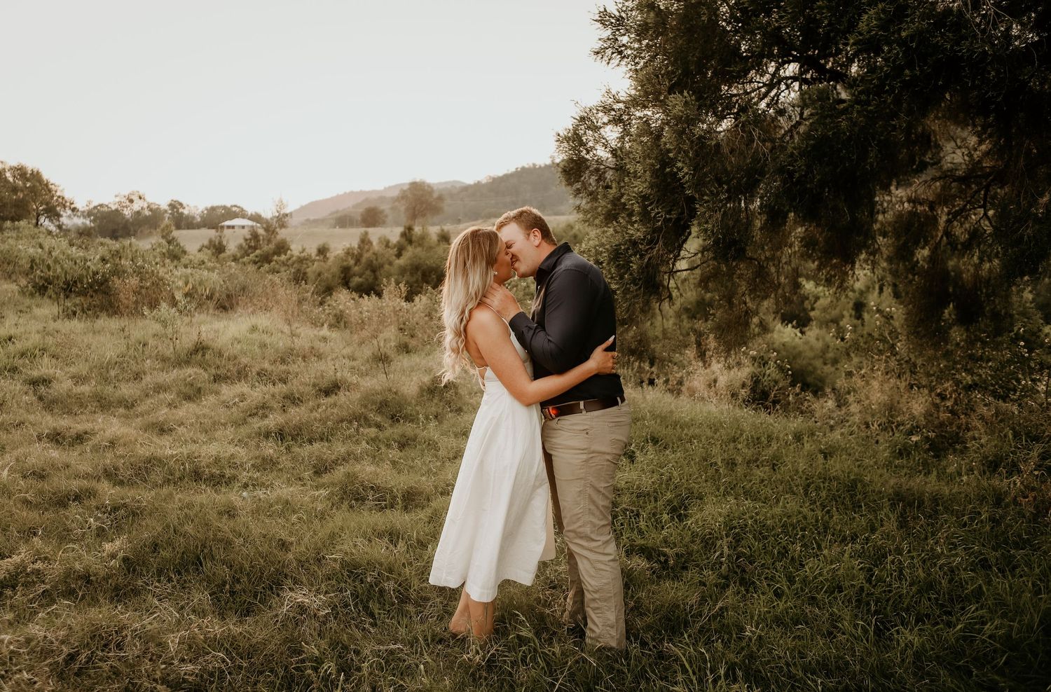 A romantic couple embraces in a sunlit meadow during a golden hour photography session.