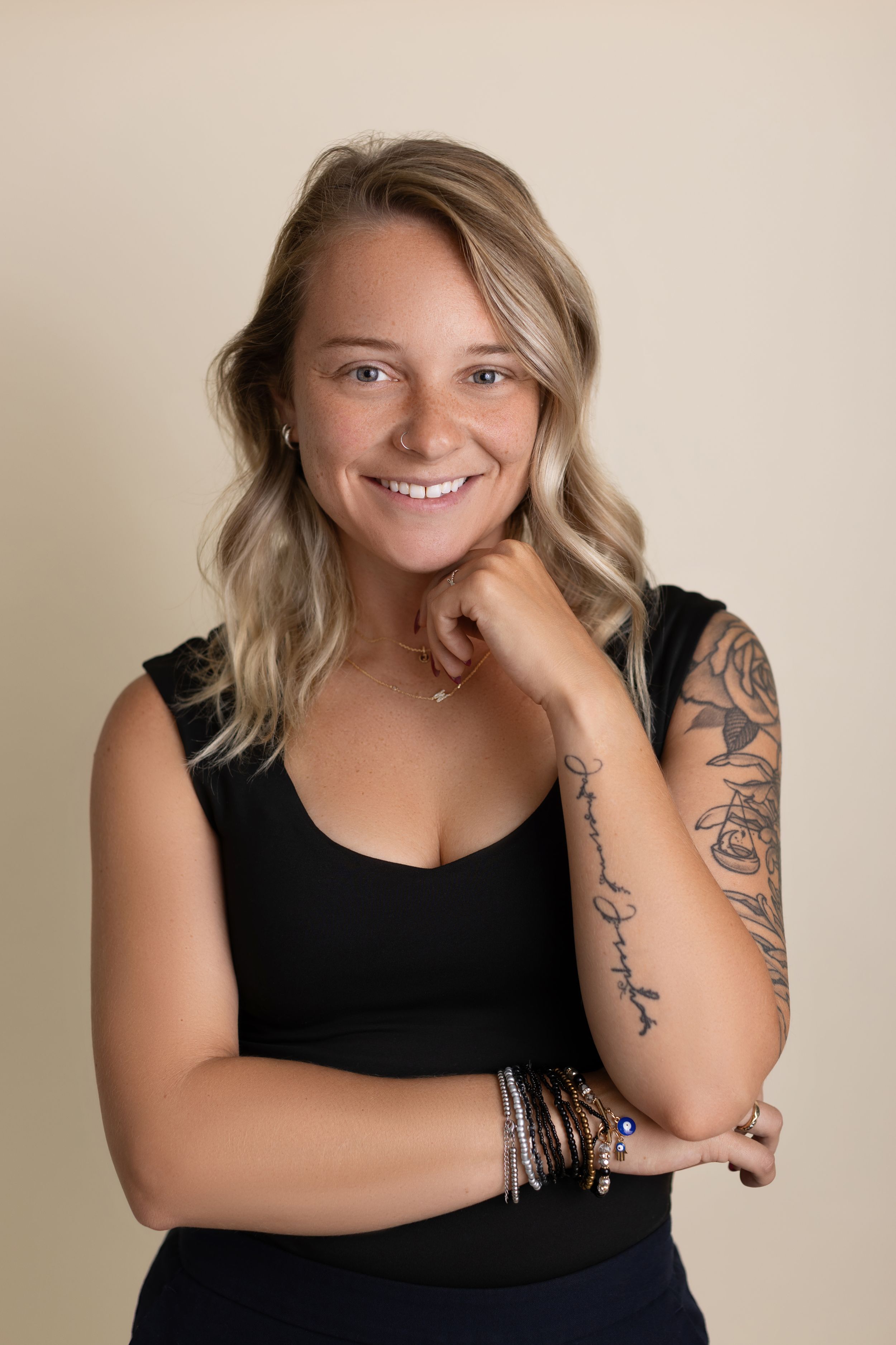 Professional portrait series showing a person in a black sleeveless top with visible arm tattoos against a neutral background.