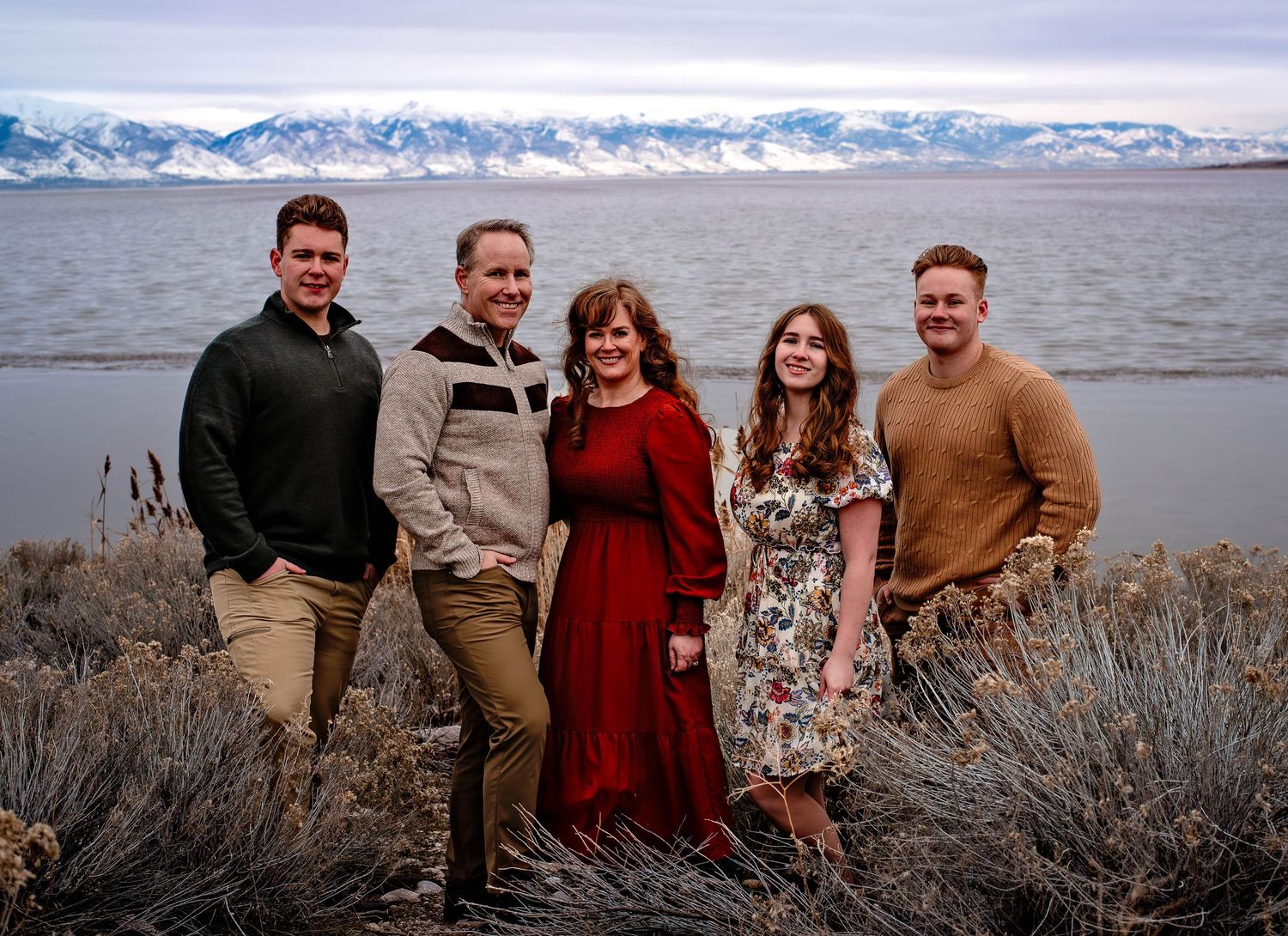 Family with the lake and snowy mountains in the background looking into the camera.