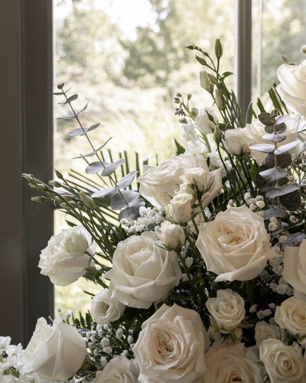 A romantic arrangement of white roses and delicate greenery displayed in soft natural window light.