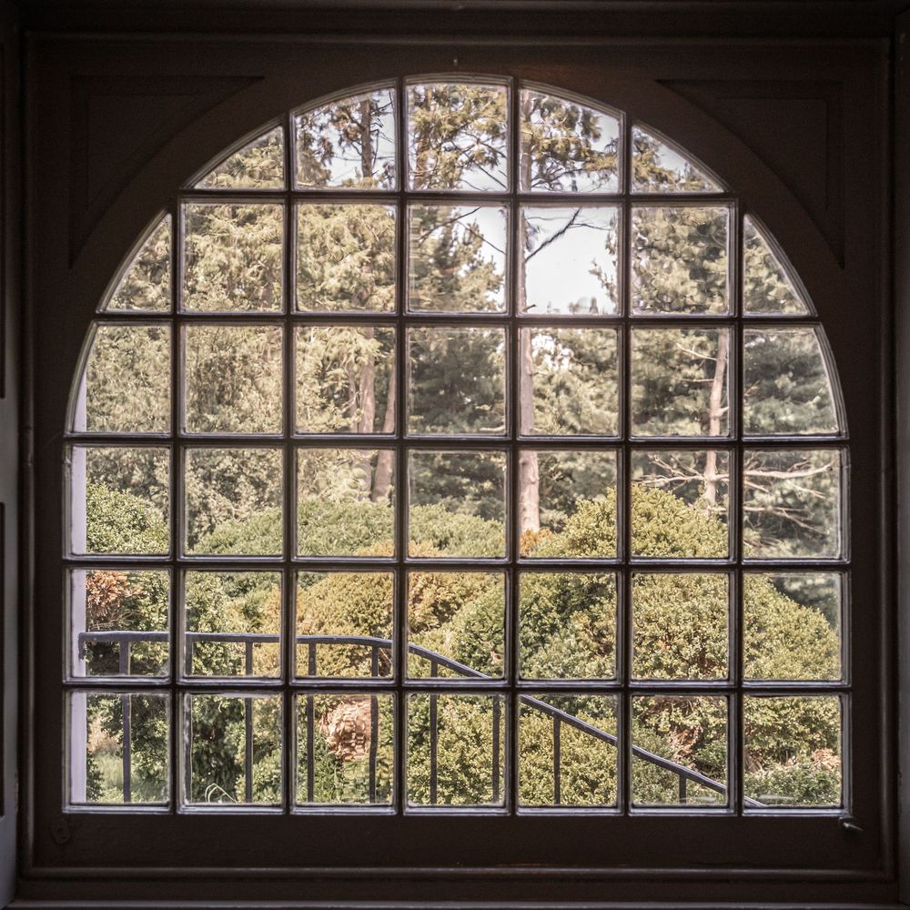 Large arched windows with grid pattern panes overlooking trees and greenery in natural daylight.