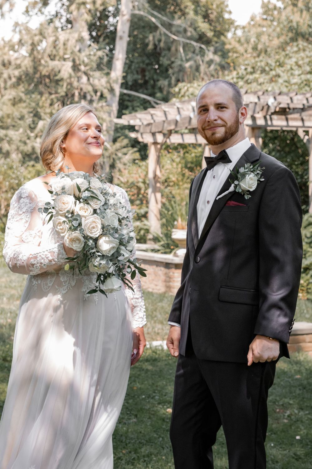 A joyful wedding couple shares candid moments in an outdoor garden setting with white flowers and greenery.