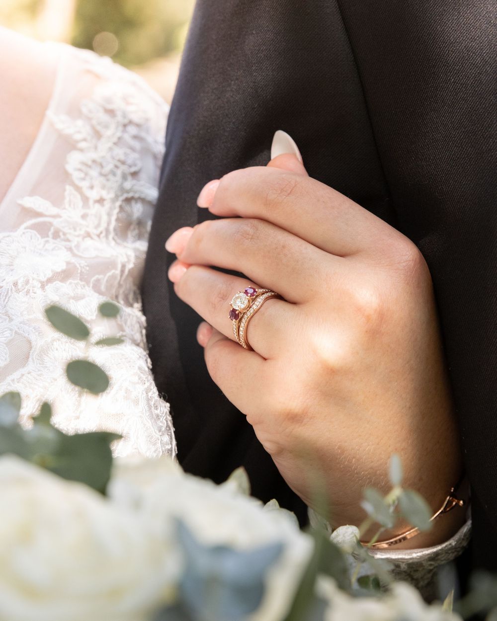Close-up view of hands wearing an elegant diamond engagement ring against a soft floral background.