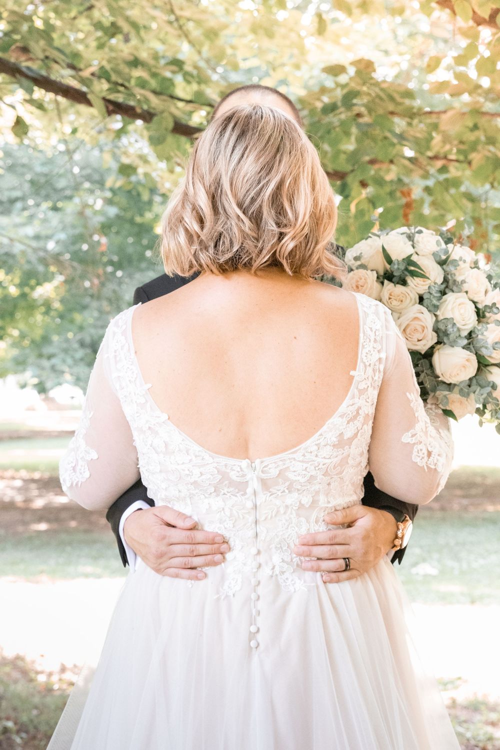 Close up details of a white lace wedding dress back with buttons and floral embroidery in an outdoor garden setting.