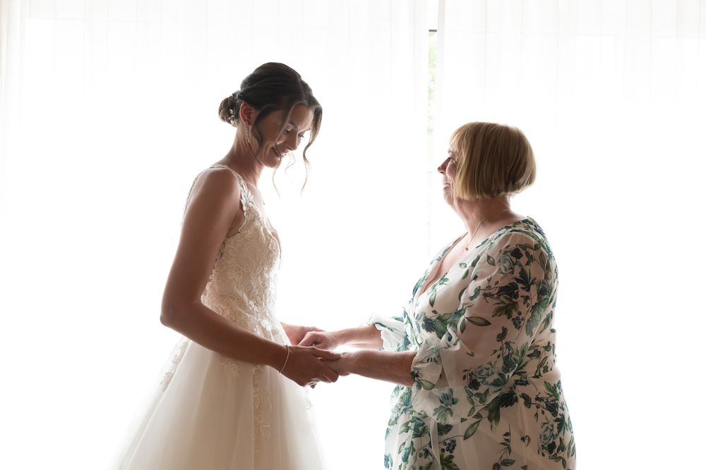 A bride and mother share an intimate moment while getting ready for the wedding ceremony in natural window light.