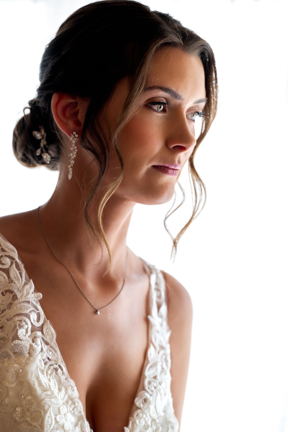 Bride wearing white lace wedding dress with plunging neckline and delicate floral details in soft natural lighting.