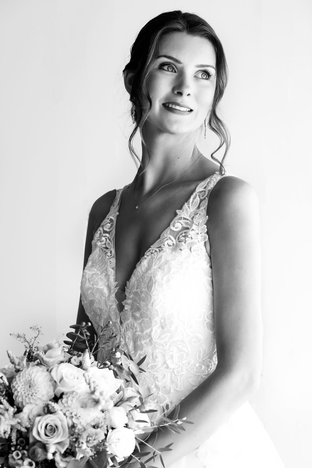 Black and white portrait of a bride in a lace V-neck wedding dress holding a bouquet of white roses and flowers.