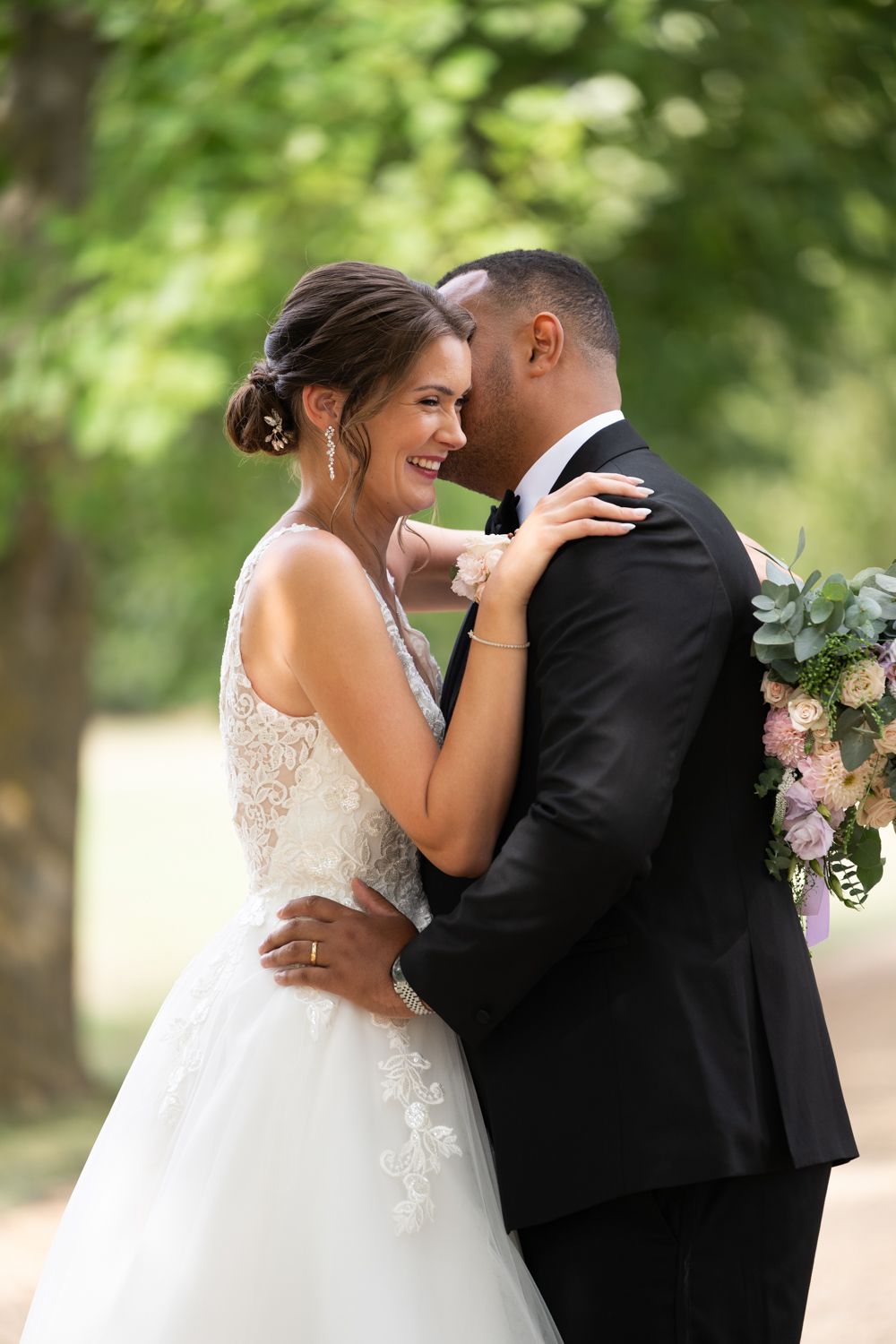A romantic wedding moment captured outdoors with a beautiful white lace gown and classic black tuxedo.