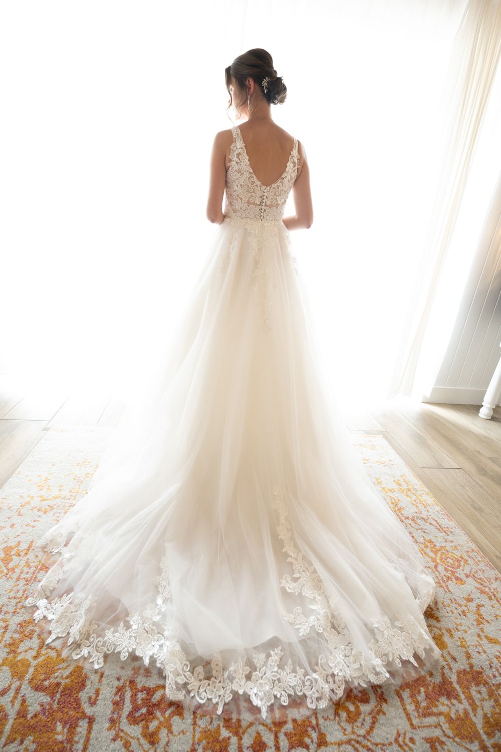 Elegant wedding dress with lace details and flowing tulle train displayed against a light-filled room.