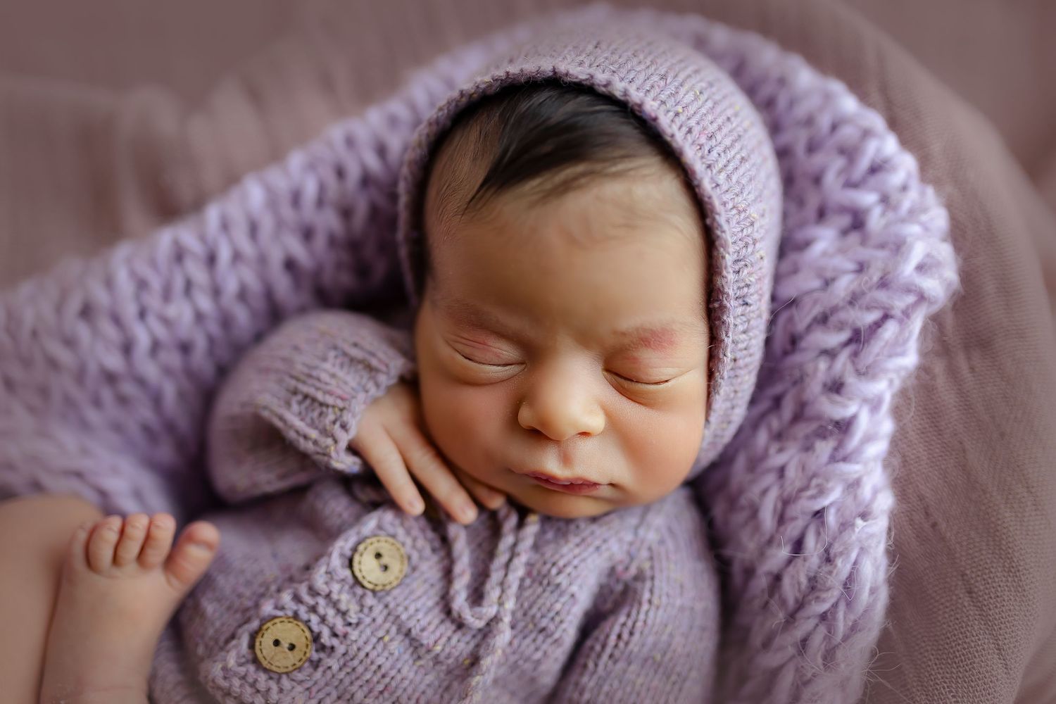 Imagen de bebe recien nacida de cera durmiendo con la manita en la cara, vestida de color lavanda