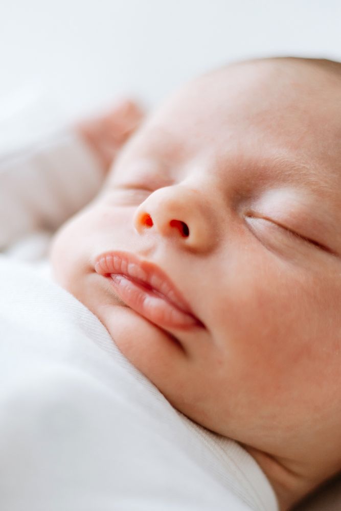 Close up of a sleeping baby's face with soft features and peaceful expression resting on white bedding.