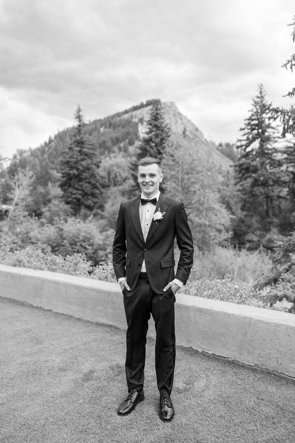 Black and white portrait on grassy hill with mountain landscape in background.