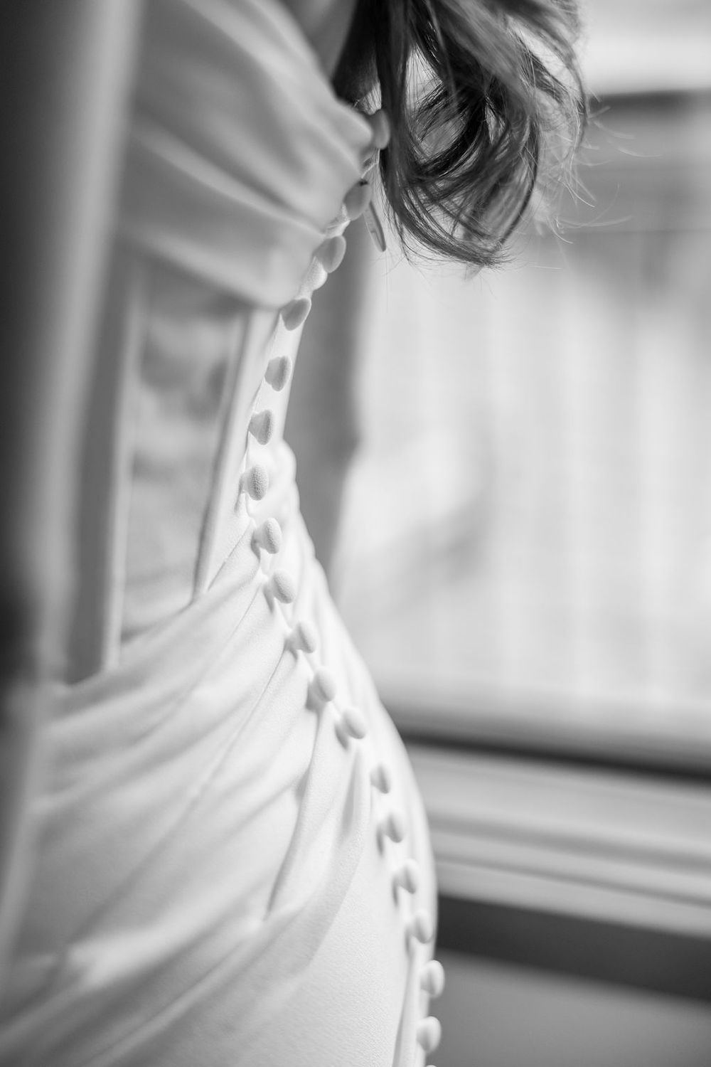 Close-up black and white detail of a white wedding dress corset with delicate button closures along the back.