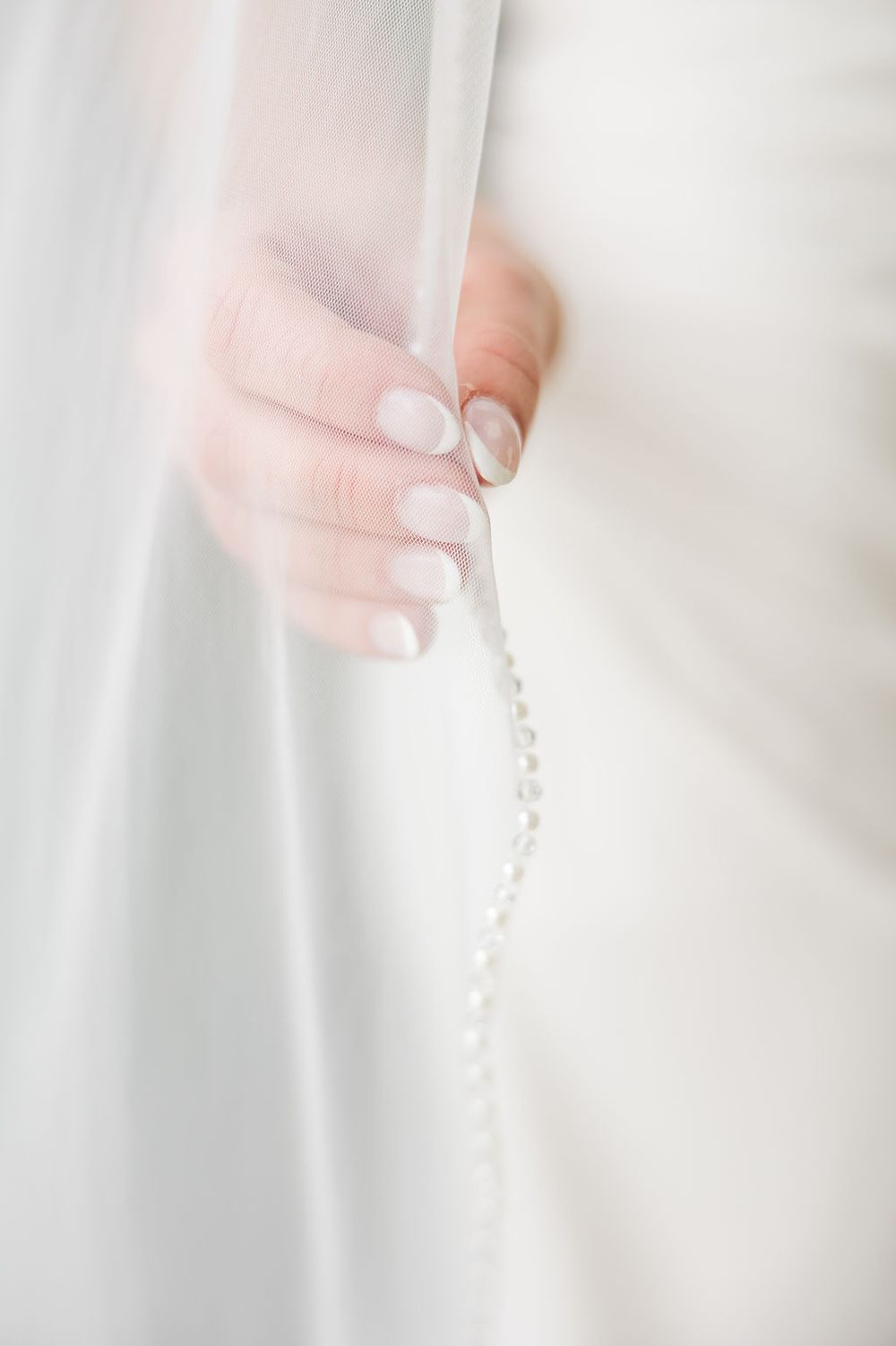 A delicate string of pearls is held against a soft white background creating an elegant bridal detail.