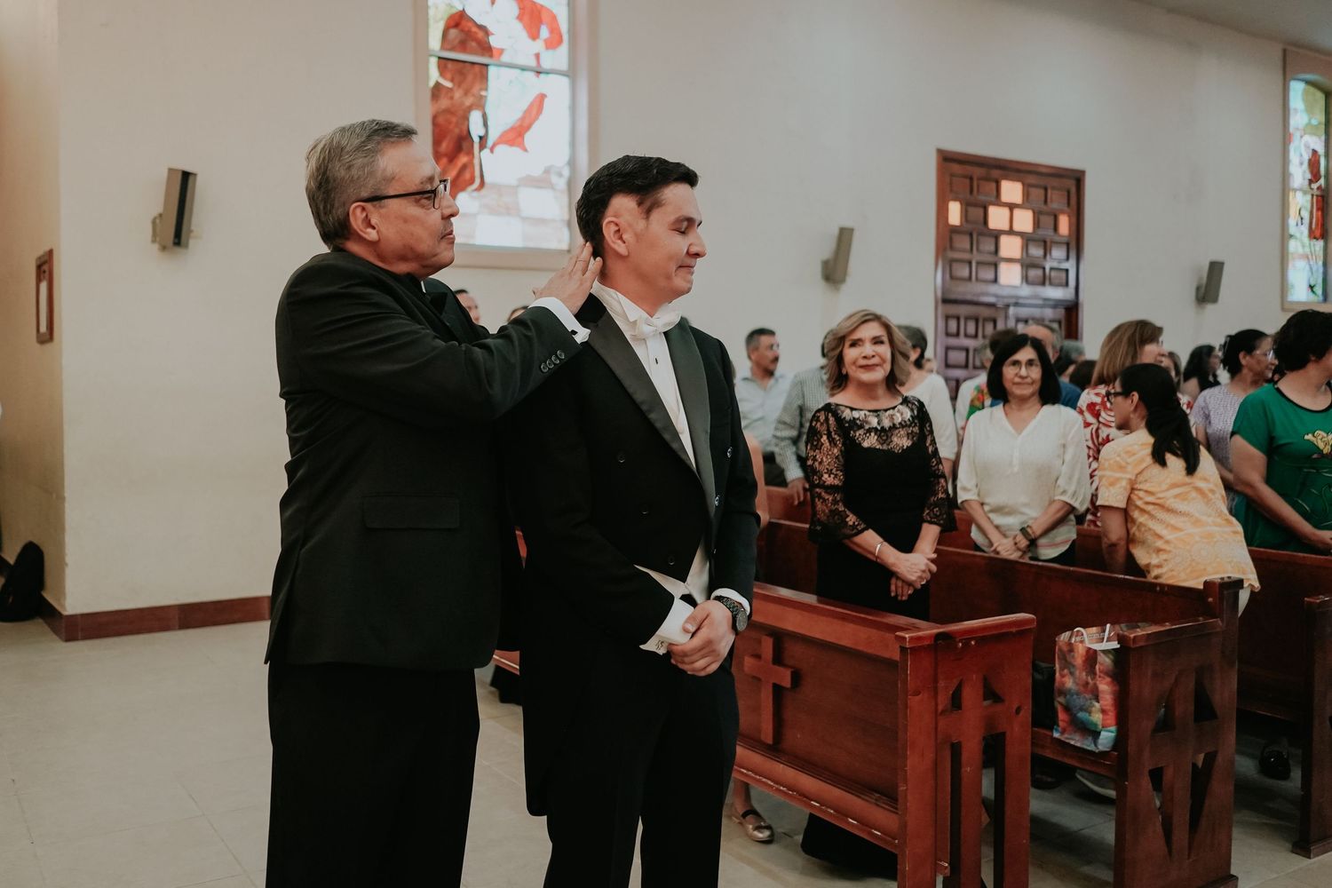 People gathered in a church or chapel setting with wooden pews during what appears to be a service or ceremony.