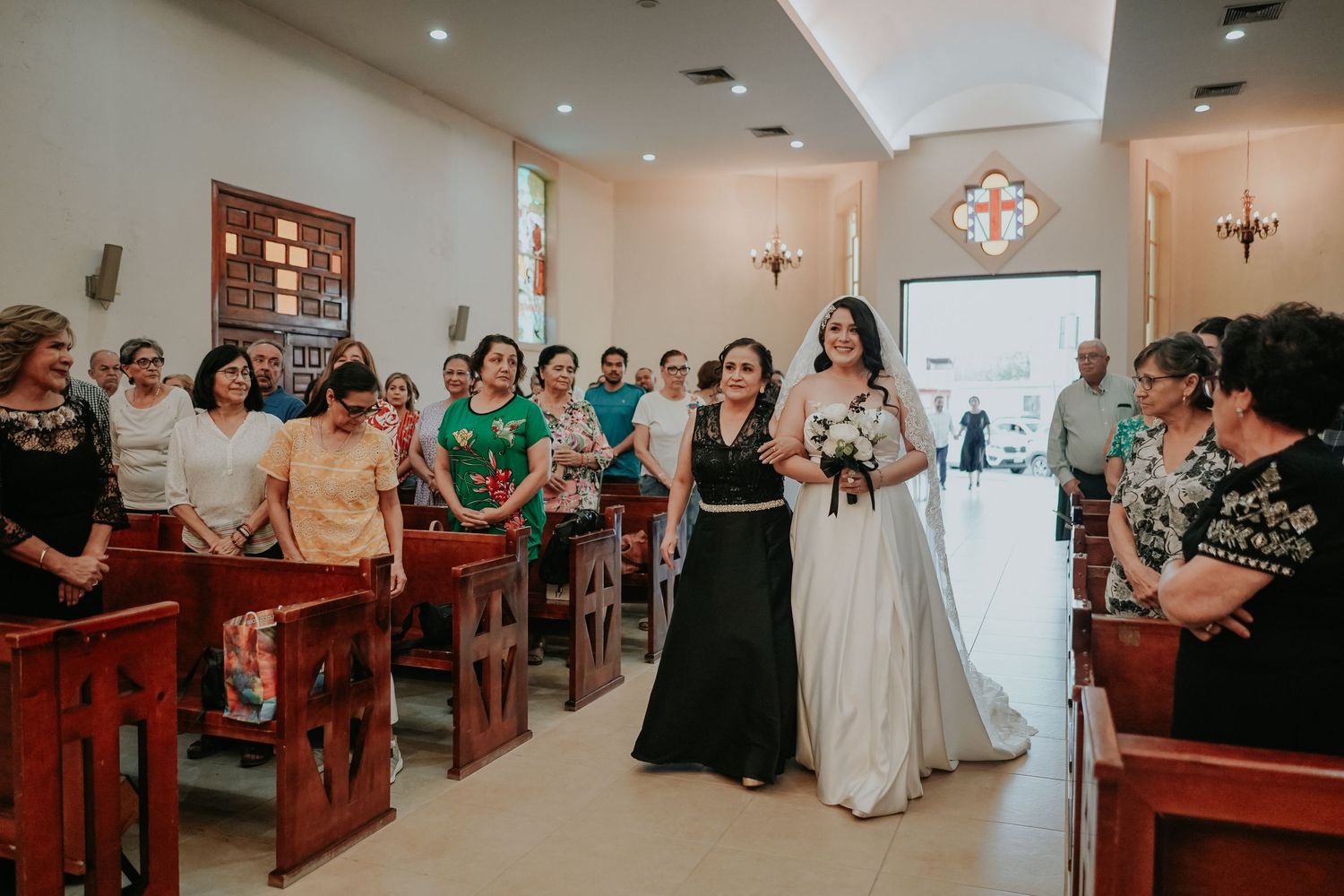 A wedding ceremony takes place in a traditional church with guests seated in wooden pews.