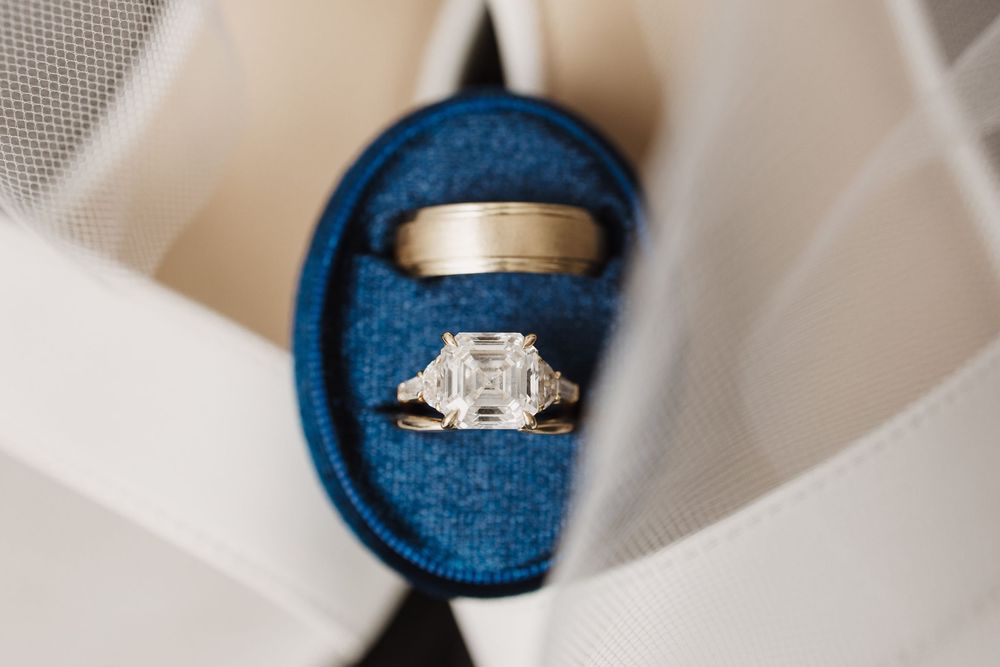 A platinum engagement ring with a princess cut diamond center stone and channel set side stones sparkles against a blue backdrop.
