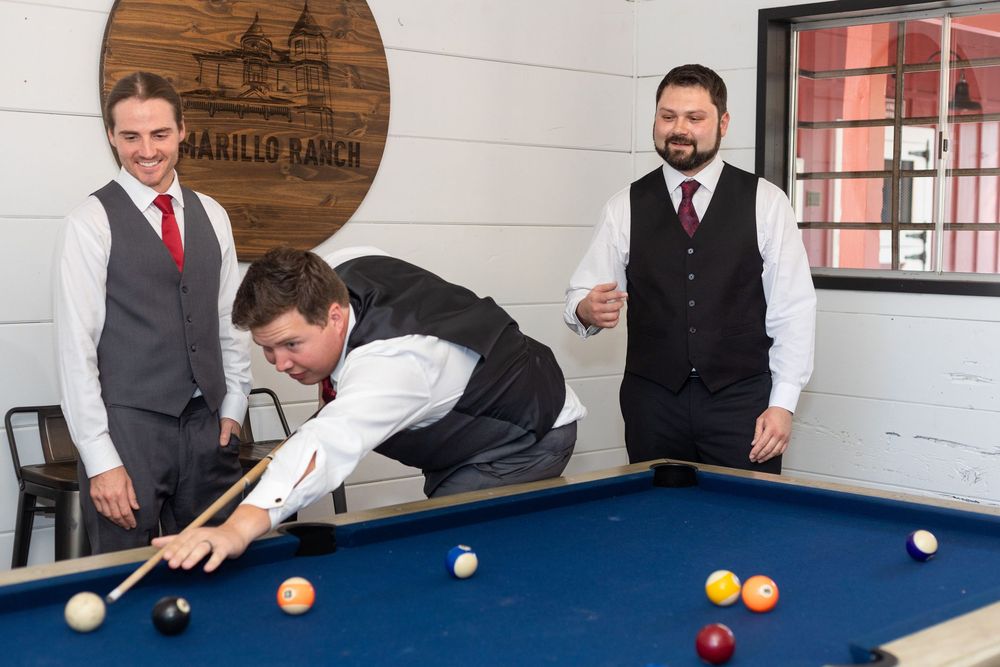 Three people in formal attire playing pool together at a game room with a rustic wooden sign on the wall.