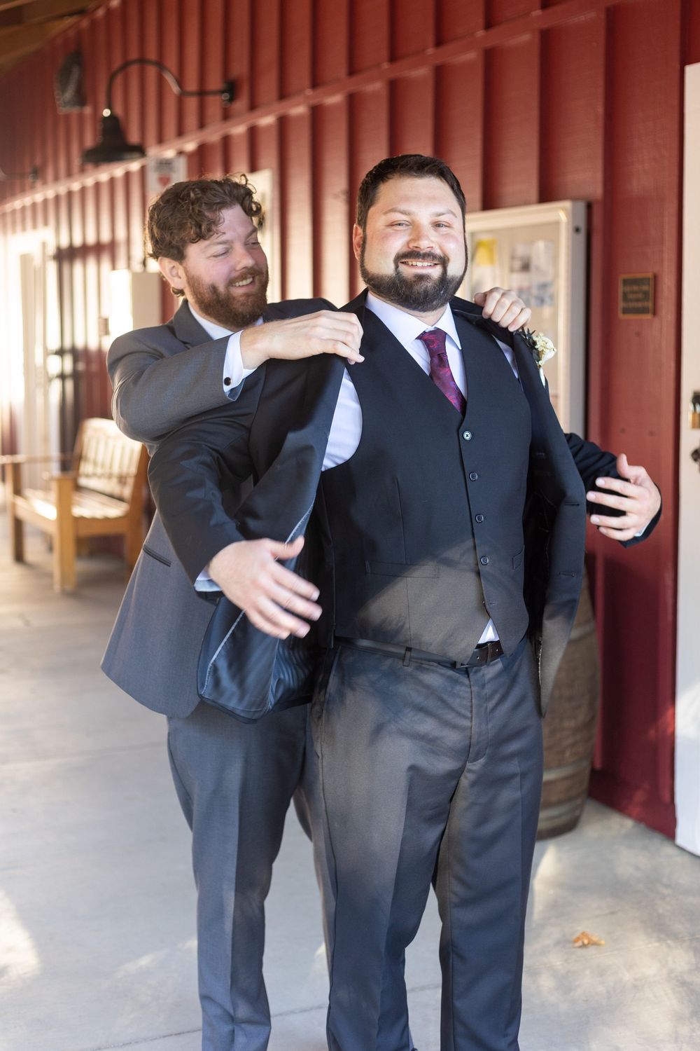 Groomsmen in black suits share candid moments and laughter while walking through a covered outdoor hallway.