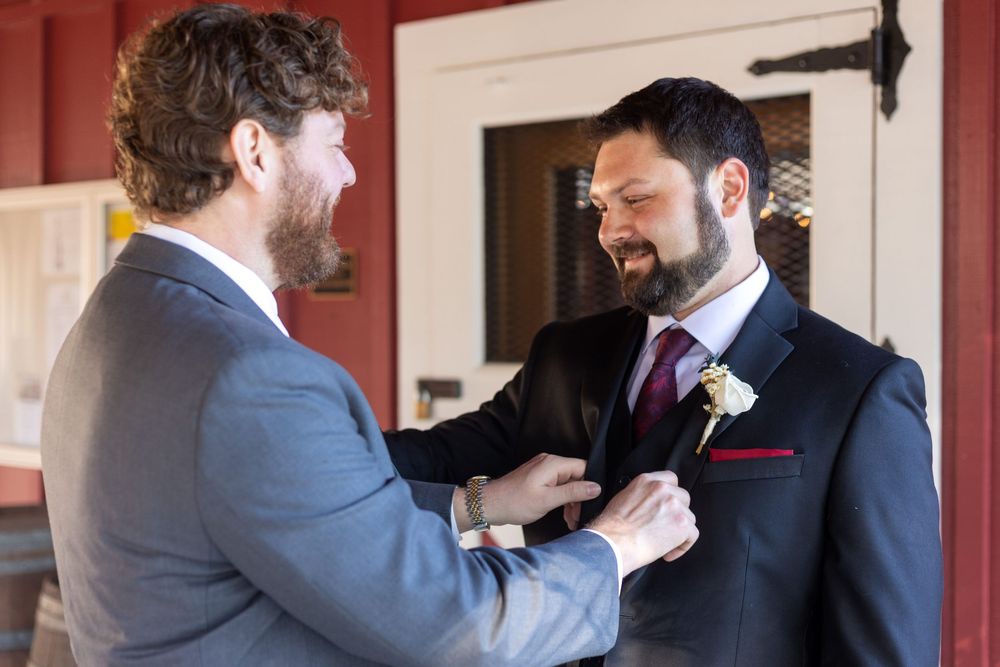 A groomsman helps adjust another groomsman's boutonniere in a formal wedding setting.