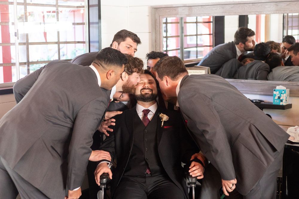 A group of people in dark suits laugh and interact during what appears to be a social gathering.