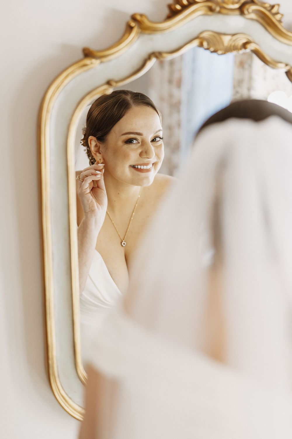 A series of elegant mirror reflections showing a person putting on jewelry in an ornate gold-framed mirror.