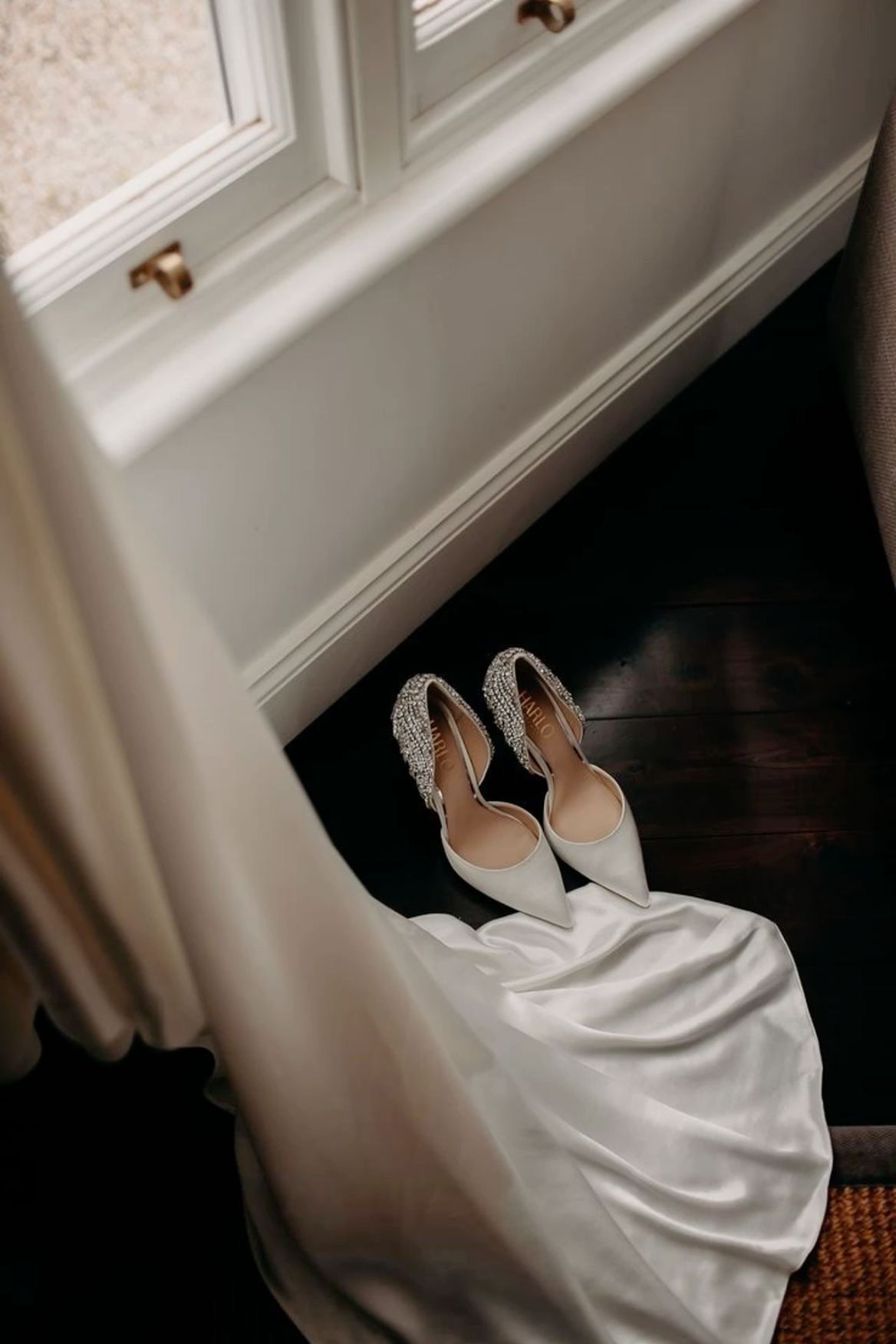 White wedding dress and shoes arranged elegantly by a window with natural lighting.