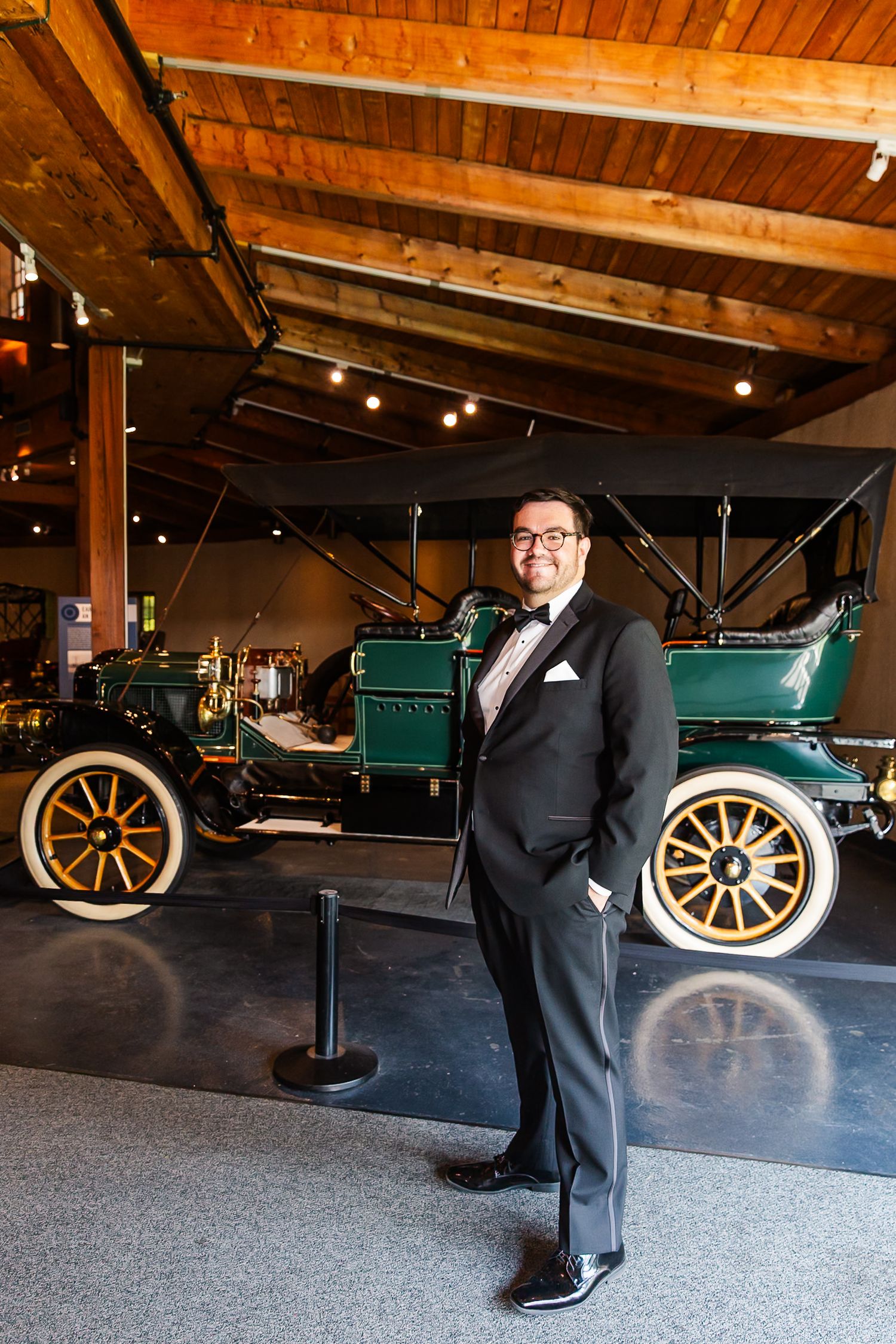 Classic green vintage car on display in museum with wooden beam ceiling and track lighting.