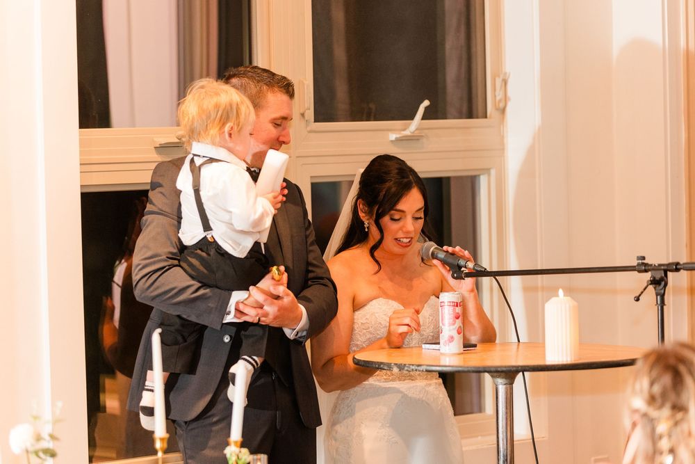 Wedding guests enjoy a lively reception dinner in an elegant white-columned venue with warm lighting.