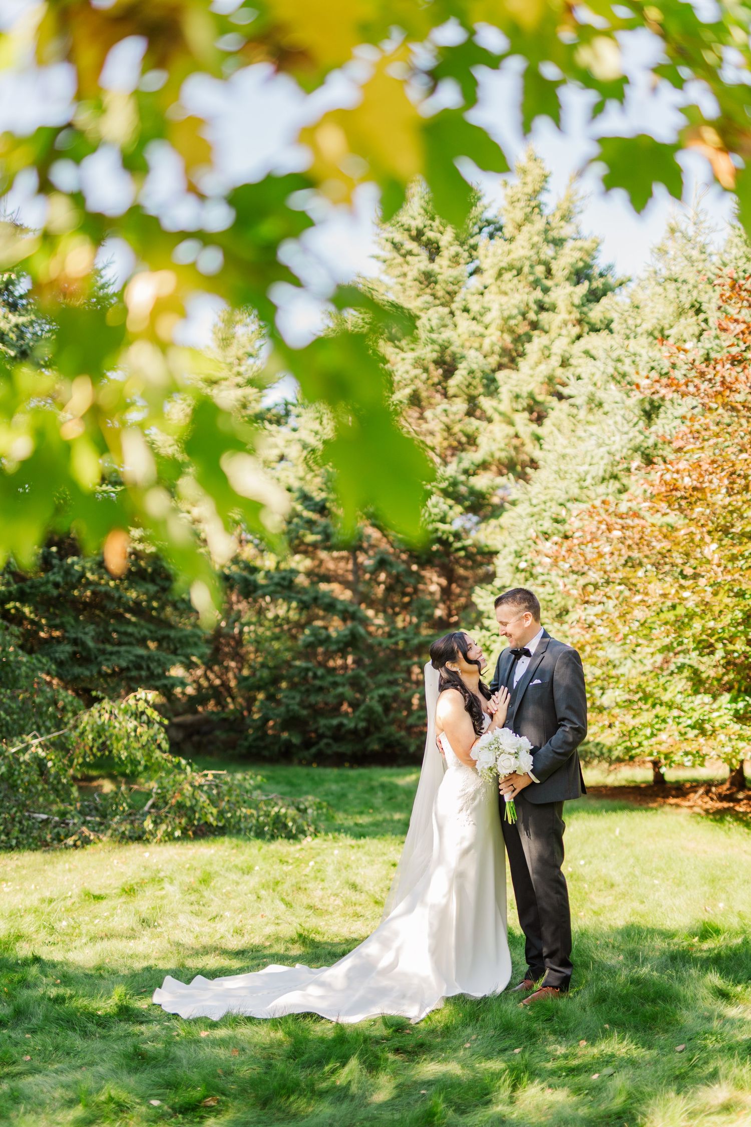 A couple shares a romantic moment on a hillside with colorful fall foliage and evergreen trees in the background.
