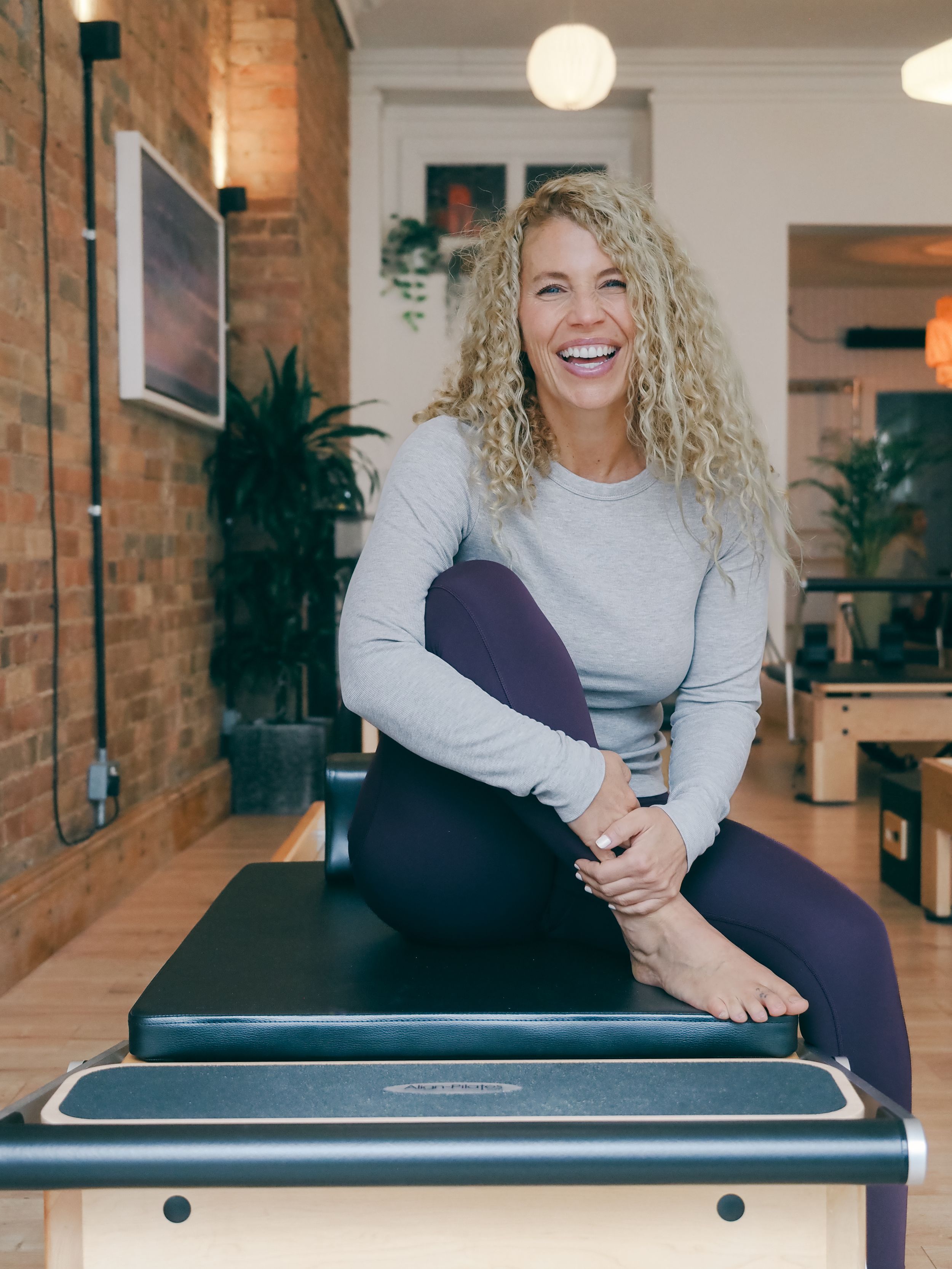 Fitness trainer in athletic wear sitting on exercise equipment in a modern studio with brick walls.