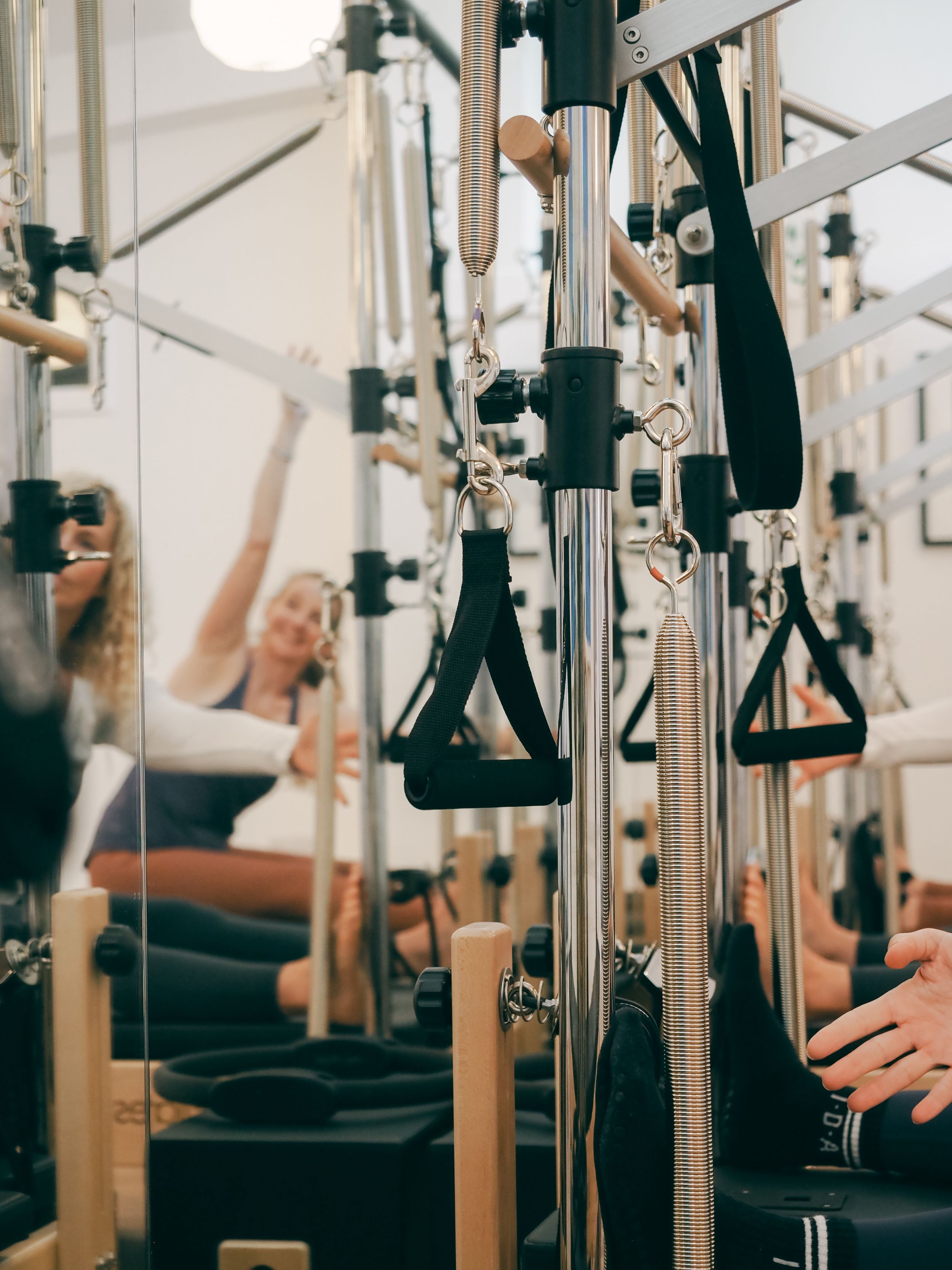 People exercising on Pilates reformer machines in a bright modern fitness studio during a workout class.