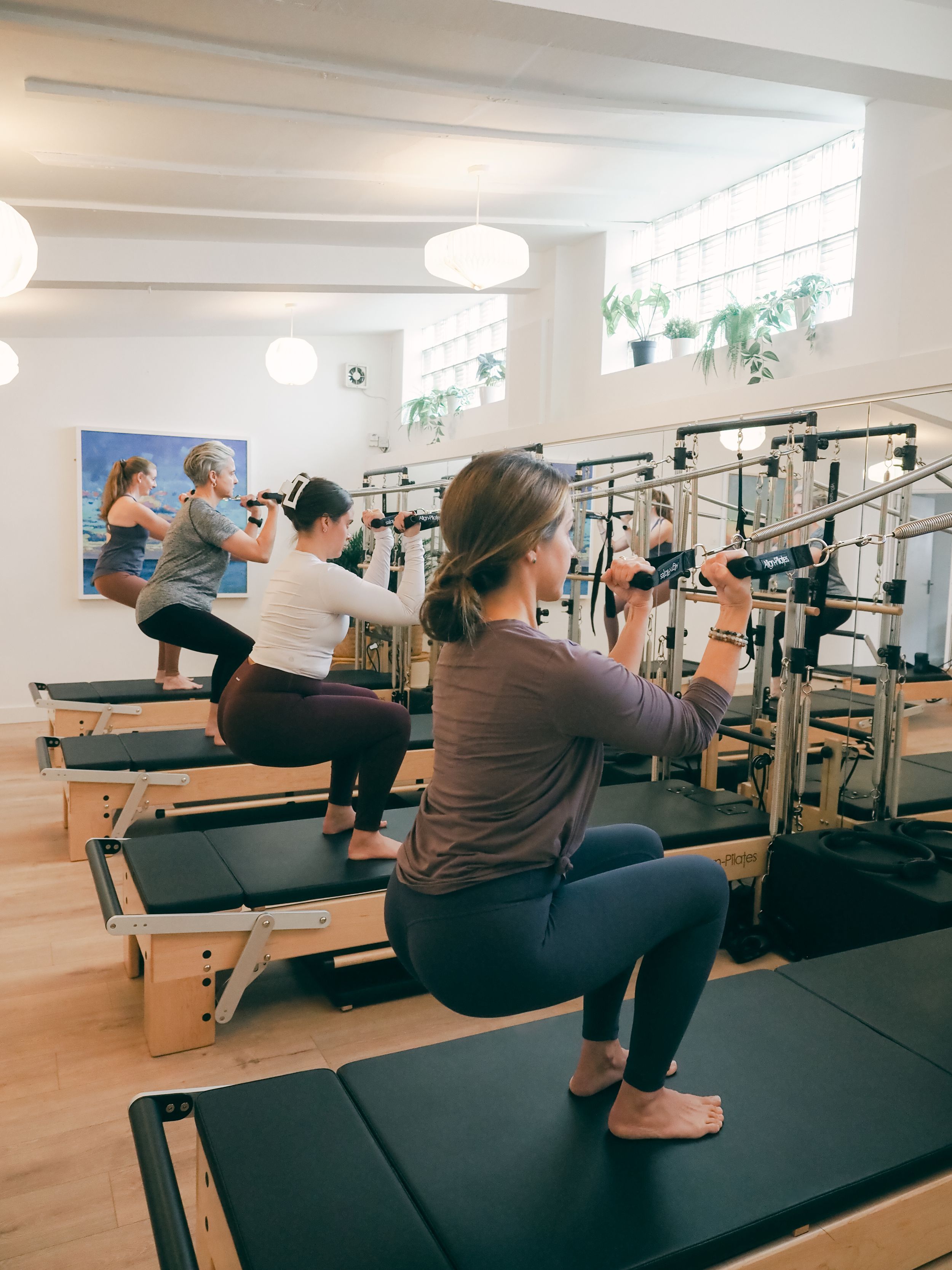 Students practicing exercises on reformer machines during a Pilates class in a bright, modern fitness studio.