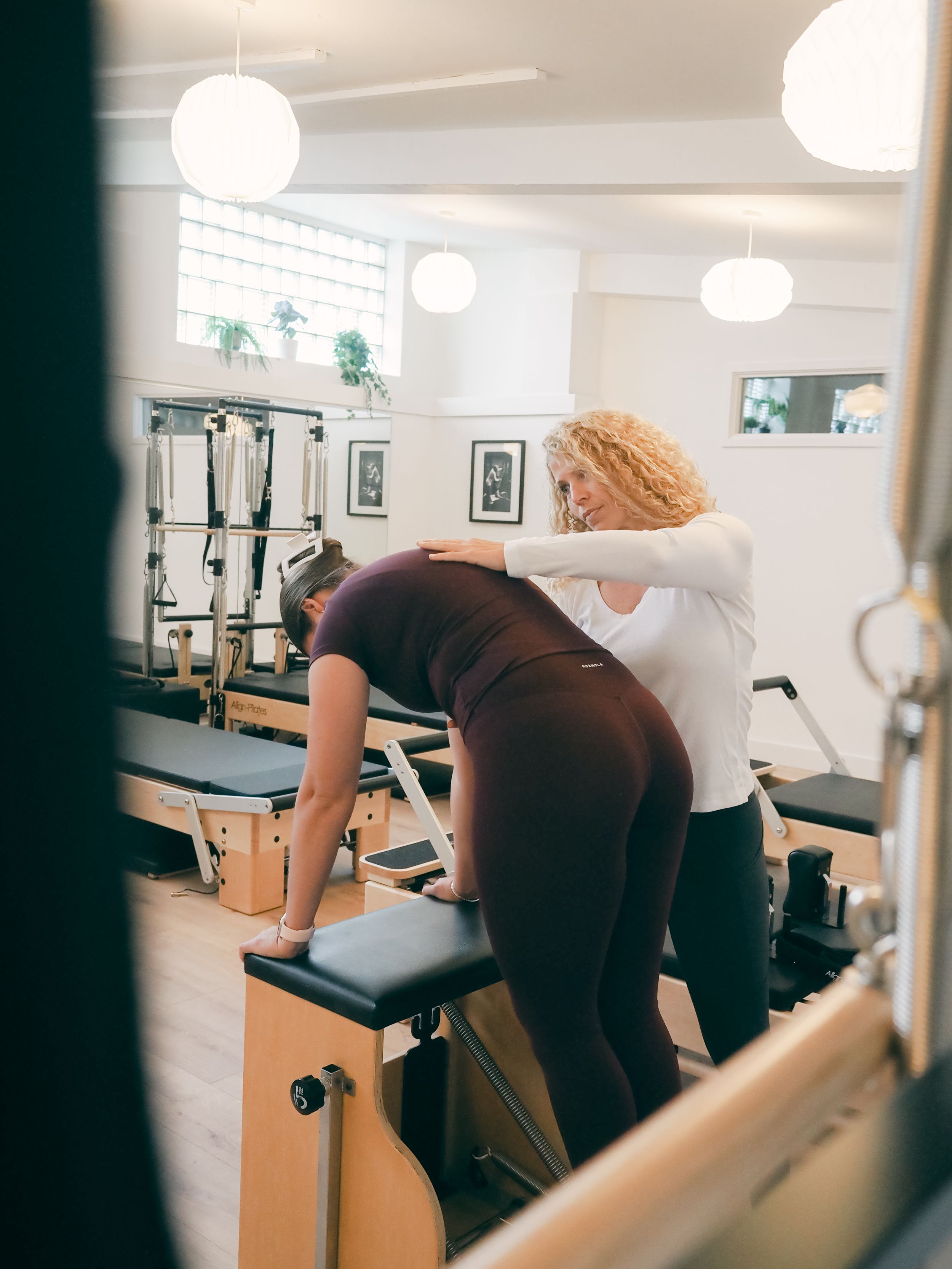 Instructor assisting student with proper form during a Pilates reformer exercise in a modern studio.