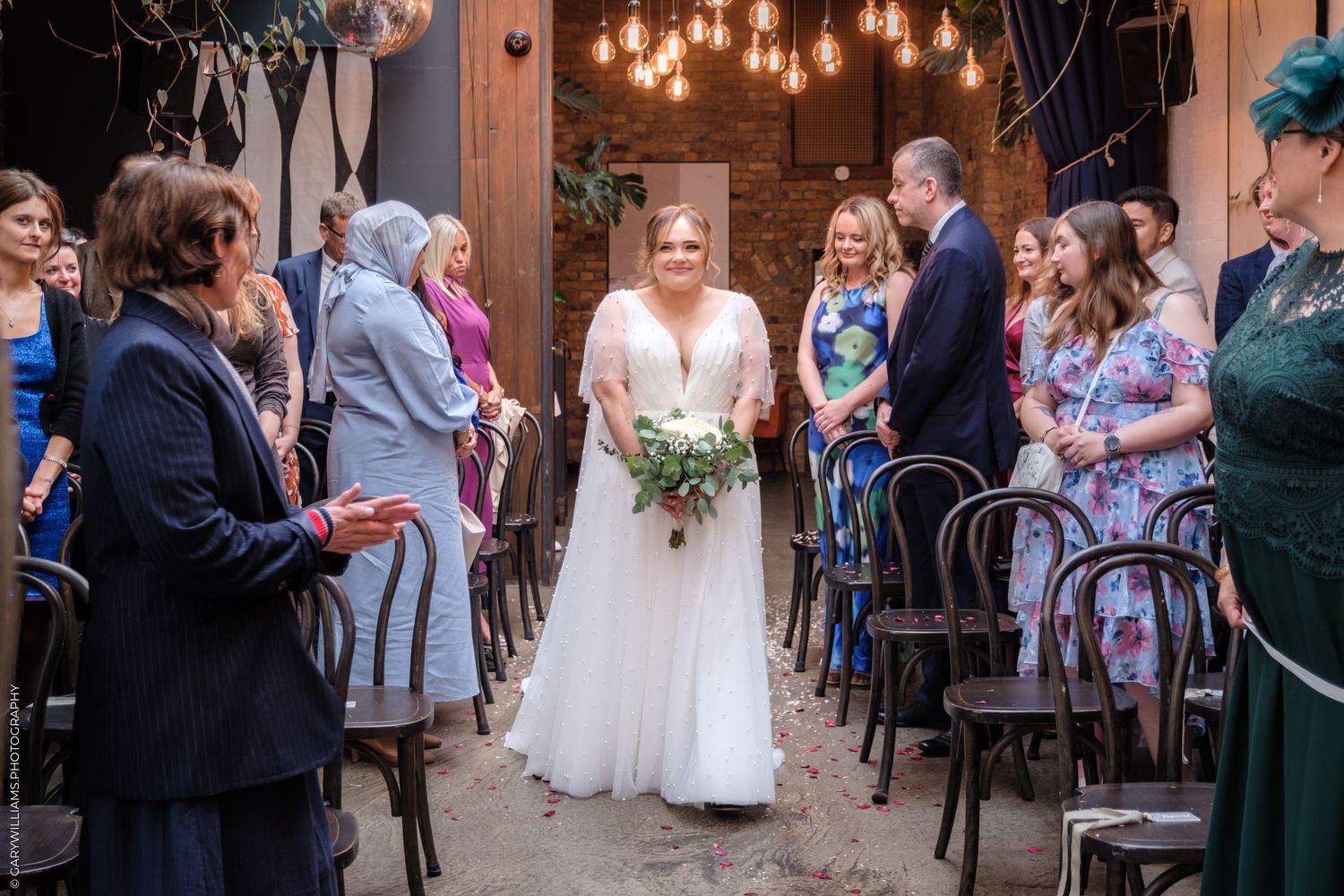 A group of wedding guests dance together under warm lighting at a rustic barn reception venue.